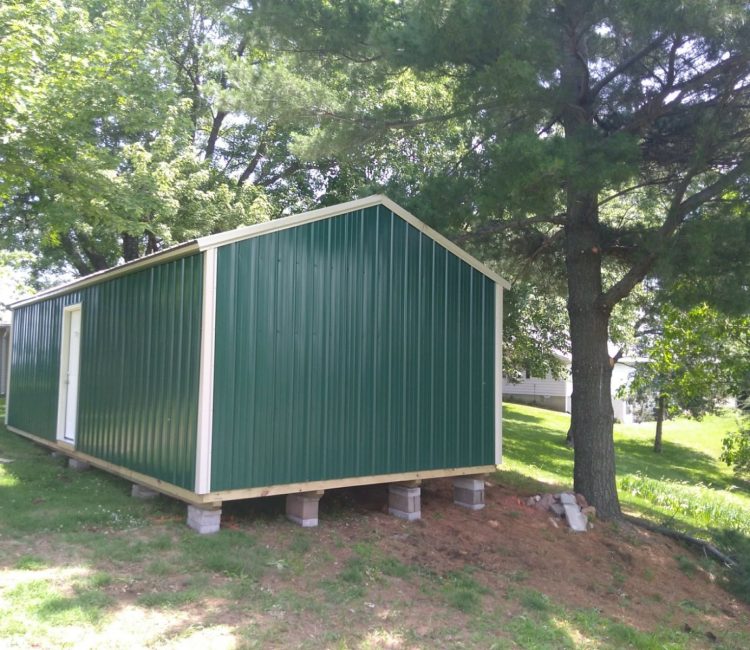 Green storage shed on blocks in residential backyard
